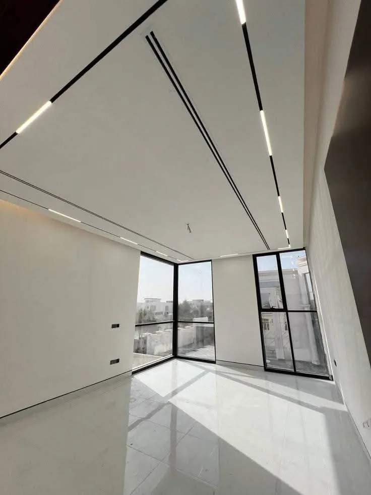 Empty bright room with slim recessed linear lights running across a white ceiling